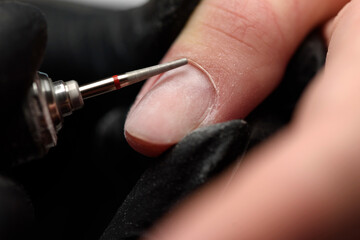 Professional hardware manicure on an electric machine in a nail salon. The process of lifting the cuticle with a cutter close-up. Master uses an electric nail file drill to trim and remove cuticles.