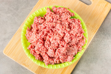Chopped minced meat in a green plastic plate on a wooden cutting board. View from above.