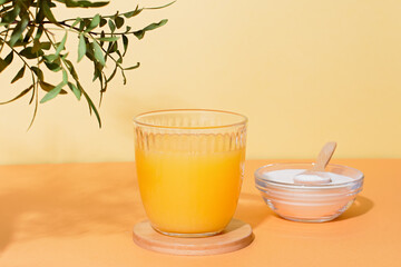Orange juice glass and collagen powder on table with plant and shadow