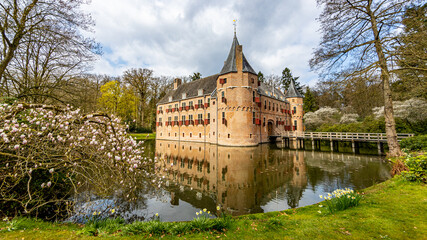 Fototapeta premium Het Oude Loo castle with its bridge, surrounded by its moat with reflection in the water and trees, sunny spring day with a blue sky and white clouds in Paleispark Kroondomein, Apeldoorn, Netherlands