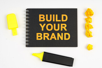 On the table is a marker, an exclamation mark and a notebook with the inscription - BUILD YOUR BRAND