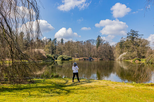 Lake With Reflection In The Water Surrounded By Bare Trees, Mature Woman With Back To Camera Admiring The Place, Sunny Spring Day In Paleispark Kroondomein Het Loo In Apeldoorn, Netherlands