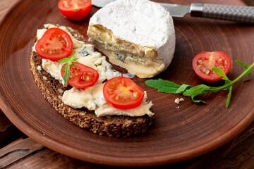 Cereal bread with blue cheese and cherry tomatoes on a clay plate on a wooden background. Healthy vegetarian food.