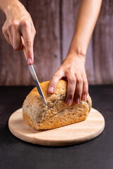 Homemade whole wheat bread fresh out of the oven. Contains many nutrients Vitamins and Nutrition good for health Hand holding a knife facing bread on a wooden cutting board. Concept Healthy food.