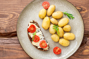 Boiled young potatoes and cereal bread with blue cheese and tomatoes on a plate on a wooden background. Vegetarian food.