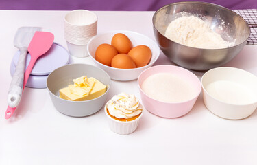 Ingredients and part of the equipment with a ready-made cake for making cupcakes on a white background. Flour, sugar, eggs, butter, spatulas, scales, milk. Selective focus.