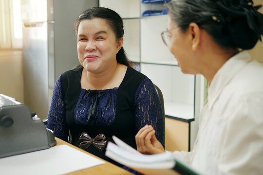 Happy Asian blind person woman with vintage braille typewriter or Brailler for people with vision disabilities, working and talking with senior colleague woman in office workplace.