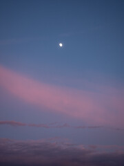 The moon in the evening blue sky with soft pink and dark gray clouds
