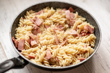 Pasta with bacon, sausage in a pan with a creamy sauce.