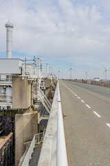 Road next to Delta Works with windmills in the background. Dams, sluices, locks, dykes, levees, and storm surge barriers. Environmental engineering in South Holland and Zeeland,  Netherlands