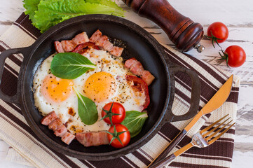 English breakfast or lunch with fried egg, spinach, arugula, tomatoes and bacon on black pan.