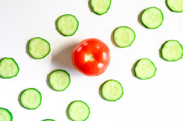 repeating pattern of sliced semicircles of fresh raw vegetable cucumbers for salad and a whole tomato in the center isolated on a white background flat lay, top view