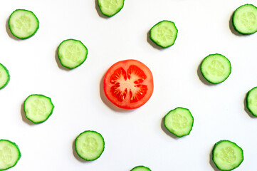 repeating pattern of sliced semicircles of fresh raw vegetable cucumbers for salad and a slice of tomato in the center isolated on a white background flat lay, top view