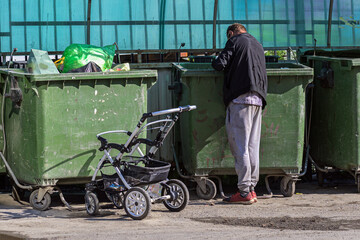 A homeless man is looking for empty cans of beer in a garbage container