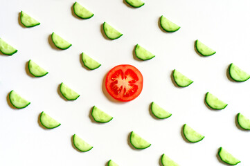 repeating pattern of sliced semicircles of fresh raw vegetable cucumbers for salad and a slice of tomato in the center isolated on a white background flat lay, top view