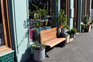 Fototapeta na wymiar Wooden Public Bench & Planters on Sunny Pavement Outside Shop 