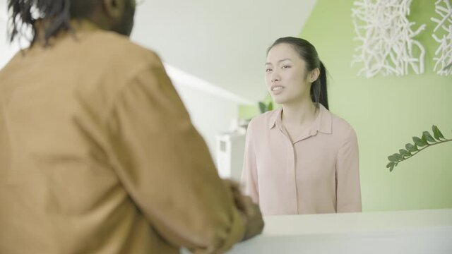 Asian female hotel administrator listening to male guest inquiry, cannot help
