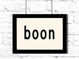 Black frame hanging on white brick wall with inscription boon © iushakovsky