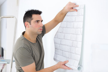 handyman putting up wallpaper on the white walls