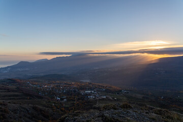 Fototapeta premium The rays of the setting sun illuminate the mountain valley from under blue clouds