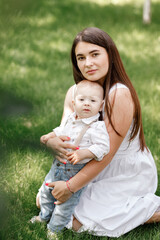 Fototapeta premium Happy beautiful woman, young mother playing with her adorable baby son, cute little boy, enjoying together a sunny warm day playing on the lawn in a summer garden