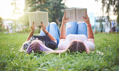 Teenagers reading books together in a university campus while lying in grass - Millennials learning...