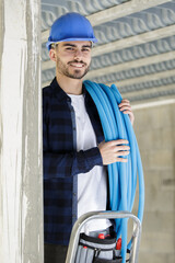 a young electrician holding rolled pipes