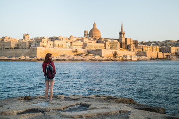 Landscape of Valetta skyline in Malta with tourist woman on the shore. The stunning skyline, Valletta churches and towers, its historic remparts from the Northern Harbour © Julien