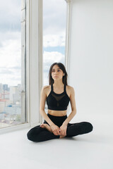 Fototapeta premium pretty armenian woman meditating in lotus pose on white floor near window