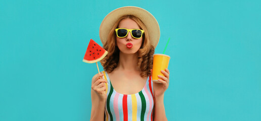 Summer colorful portrait of beautiful young woman blowing her lips with cup of juice and lollipop or ice cream shaped slice of watermelon wearing a straw hat on blue background