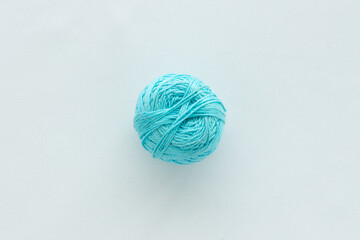 One round ball of blue color in the center of the frame on a white woven background on the theme of hand-made hobby knitting