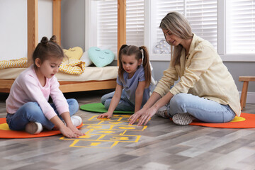 Mother and little girls taping sticker hopscotch on floor at home