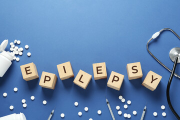 Wooden cubes with word Epilepsy, stethoscope, pills and syringes on blue background, flat lay....