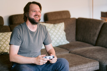 Mann spielt auf der Couch Playstation und freut sich