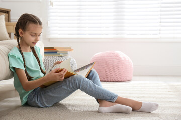 Cute little girl reading book on floor at home