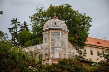 Fototapeta na wymiar Valec, Western Bohemia, Czech Republic, 19 June 2021: Green trees near glass and steel greenhouse in botanical horticultural garden, Historic pavilion in park near baroque castle at summer day