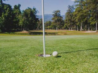 Obraz premium Photo of white golf ball on grass with hole and blue sky background
