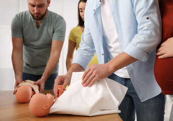 Future fathers and pregnant women learning how to swaddle baby at courses for expectant parents...
