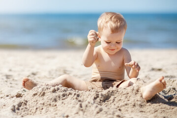 Fototapeta na wymiar A happy little boy plays with sand in the beach