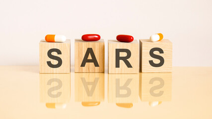 word sars is made of wooden cubes on a yellow background with pills