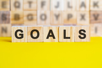 word GOALS is written on wooden cubes on a bright yellow surface, concept