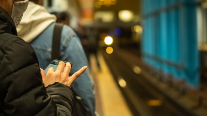 Woman in a protective mask, standing on the platform of a subway station during a pandemic ..with a mobile phone in her hands while waiting for a train