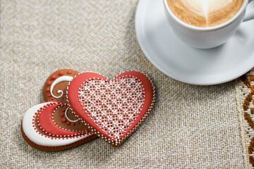 Tasty love. Top view shot of two heart shaped cookies decorated with colorful glaze near a cup of coffee
