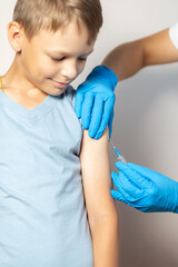Hands of a nurse in blue gloves injects a vaccine through a syringe into the shoulder of a brave...