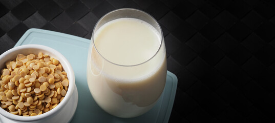 Soy milk with no sugar added in a glass on a green color plastic plate mat. Close-up images of home made healthy soy milk drink and soy beans in small bowl. Black background in a studio shot. Soymilk.