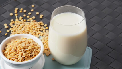 Soy milk with no sugar added in a glass on a green color plastic plate mat. Close-up images of home made healthy soy milk drink and soy beans in small bowl. Black background in a studio shot. Soymilk.