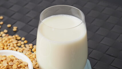 Soy milk with no sugar added in a glass on a green color plastic plate mat. Close-up images of home made healthy soy milk drink and soy beans in small bowl. Black background in a studio shot. Soymilk.