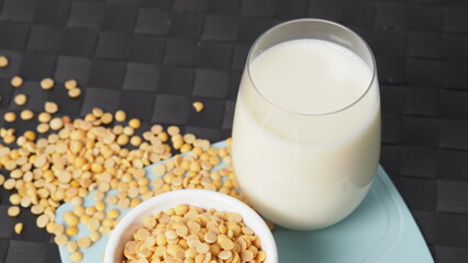 Soy milk with no sugar added in a glass on a green color plastic plate mat. Close-up images of home made healthy soy milk drink and soy beans in small bowl. Black background in a studio shot. Soymilk.