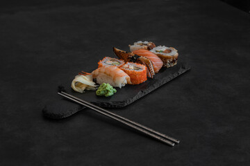 Close up of sashimi sushi and sushi roll set with chopsticks on black tray on dark background 
