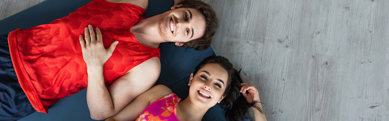 top view of young couple in sportswear lying on fitness mats and looking at camera at home, banner
